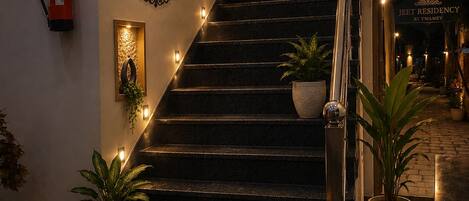 A staircase with a sign for Jeet Residency by Twamev, surrounded by potted plants and decorative lighting.