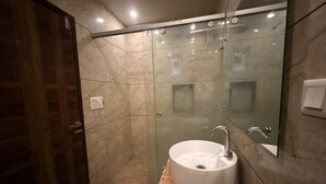 A modern bathroom with a glass-enclosed shower, a white sink, and a wooden floor. - Jeet residency by twamev (New Delhi)