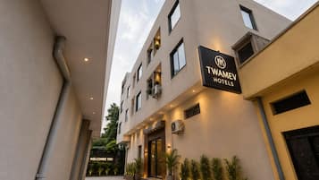 Entrada moderna de um hotel com uma placa indicando 'TWAMEV HOTELS' e uma mensagem acolhedora.
