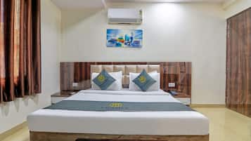 Een hotelkamer met een bed, nachtkastjes, een airconditioner, een schilderij en een logo op het beddegoed.