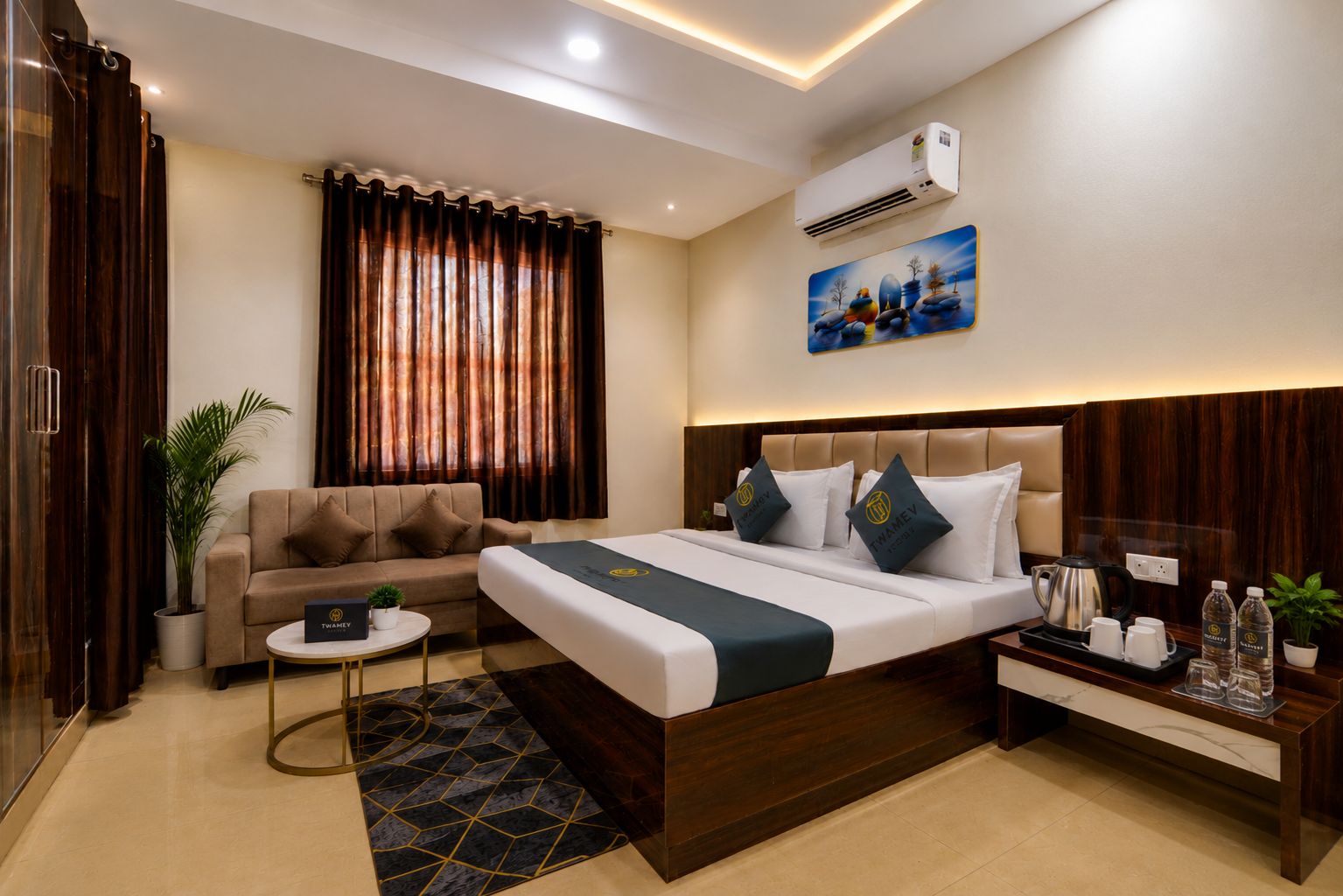 A hotel room with a bed, a sofa, a coffee table, a side table with a kettle, and a potted plant.