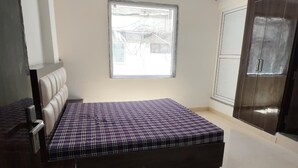 A bedroom with a bed, a window, a wardrobe, and a chair. - Jeet residency by twamev (New Delhi)