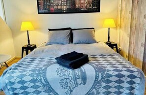 A hotel room with a bed, two bedside lamps, a cityscape artwork on the wall, and a patterned bedspread. - Lovely Apartment Wassenaar 6P (Wassenaar)