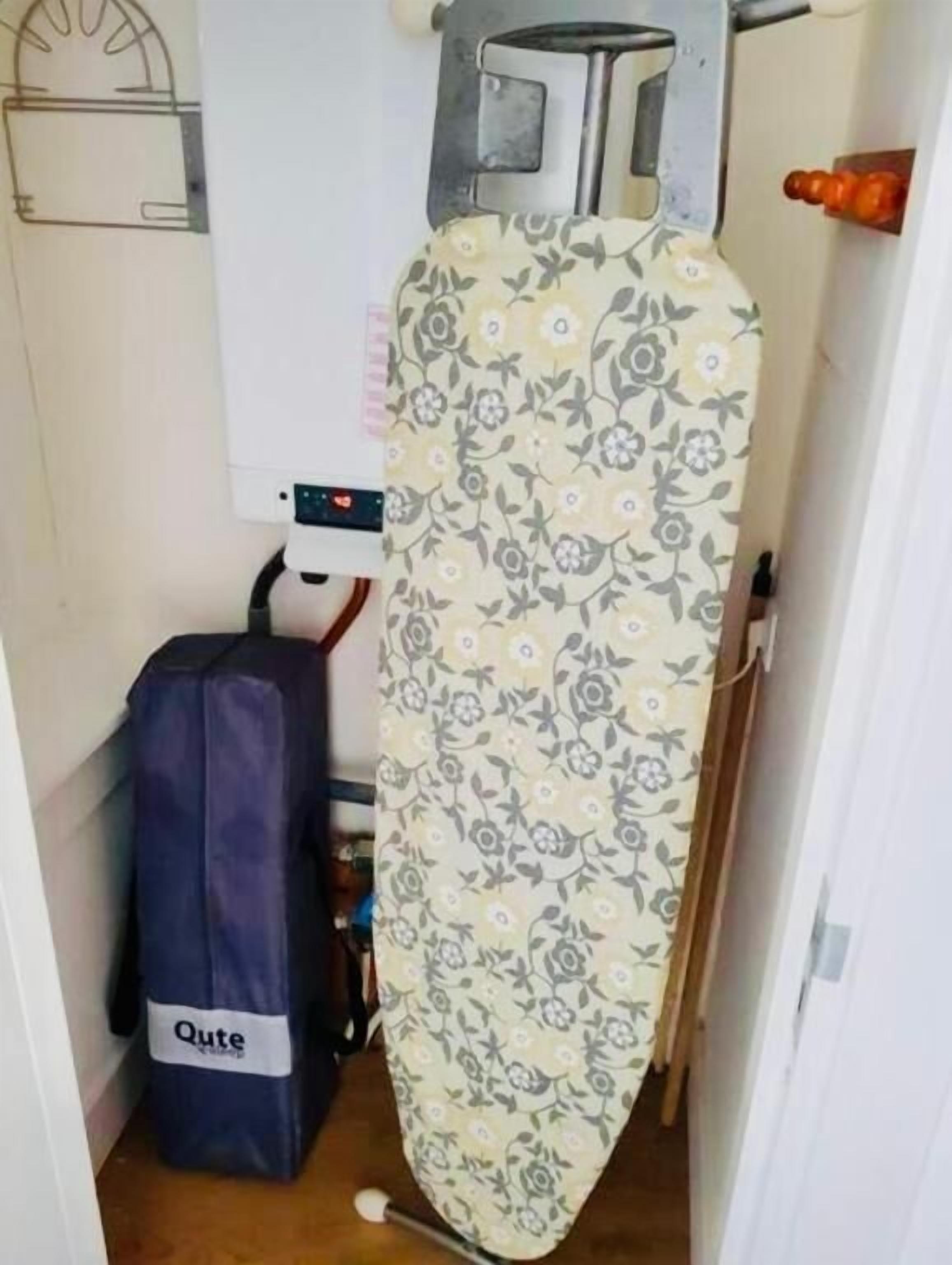 Een kleine kamer met een bed, een koffer en een strijkplank.