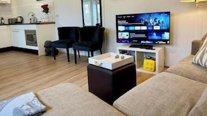 Un soggiorno moderno con una TV a schermo piatto, un divano, un tavolino da caffè e un angolo cottura sullo sfondo.
