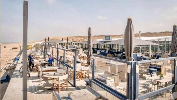 Un ristorante in riva al mare con posti a sedere all'aperto, una struttura in vetro e vista sulla spiaggia.