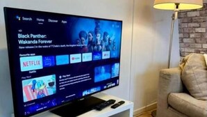 Un televisore su un mobile bianco, con telecomando, un giocattolo giallo e una libreria.