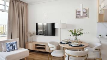 Ein modernes Wohnzimmer mit einer Couch, einem Fernseher, einem Esstisch, Stühlen und einem an der Wand befestigten Fernseher.