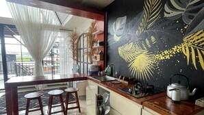 A modern kitchen with a dining area, featuring a large window, a black wall mural, and a wooden dining table. - Villa Dieng Mezzaluna (Kejajar)