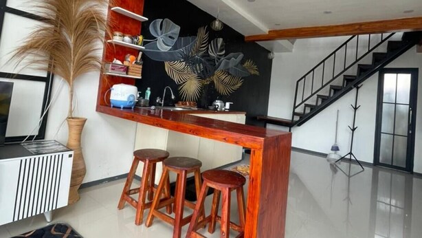A modern kitchen with a wooden bar, stools, and a decorative wall. - Villa Dieng Mezzaluna (Kejajar)