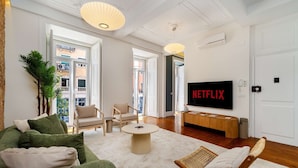 Een woonkamer met een bank, stoelen, een salontafel, een televisie en een groot raam.