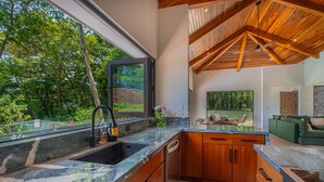A modern kitchen with a large window, wooden cabinets, and a view of the outdoors. - Modern secluded villa with private pool, jungle setting, and stunning Gulf views near Golfito. (Golfito)