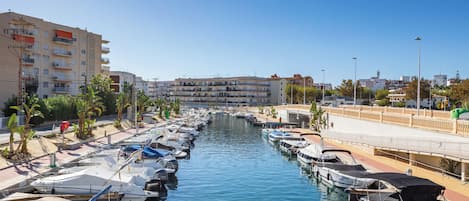 A marina with boats docked along a waterfront, surrounded by buildings and a clear sky.