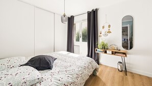 A bedroom with a bed, a bedside table with a plant, a mirror, and a window with curtains. - HAPPYFEW SUITE FABRON (Nice)