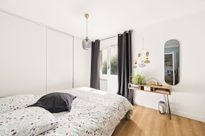 A bedroom with a bed, a bedside table with a plant, a mirror, and a window with curtains. - HAPPYFEW SUITE FABRON (Nice)
