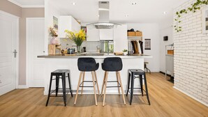 A modern kitchen with white cabinetry, a central island, two black bar stools, and a brick accent wall. - HAPPYFEW SUITE FABRON (Nice)