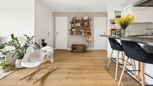 A modern kitchen with a wooden floor, a dining area with black chairs, a white rocking chair, and a bookshelf. - HAPPYFEW SUITE FABRON (Nice)