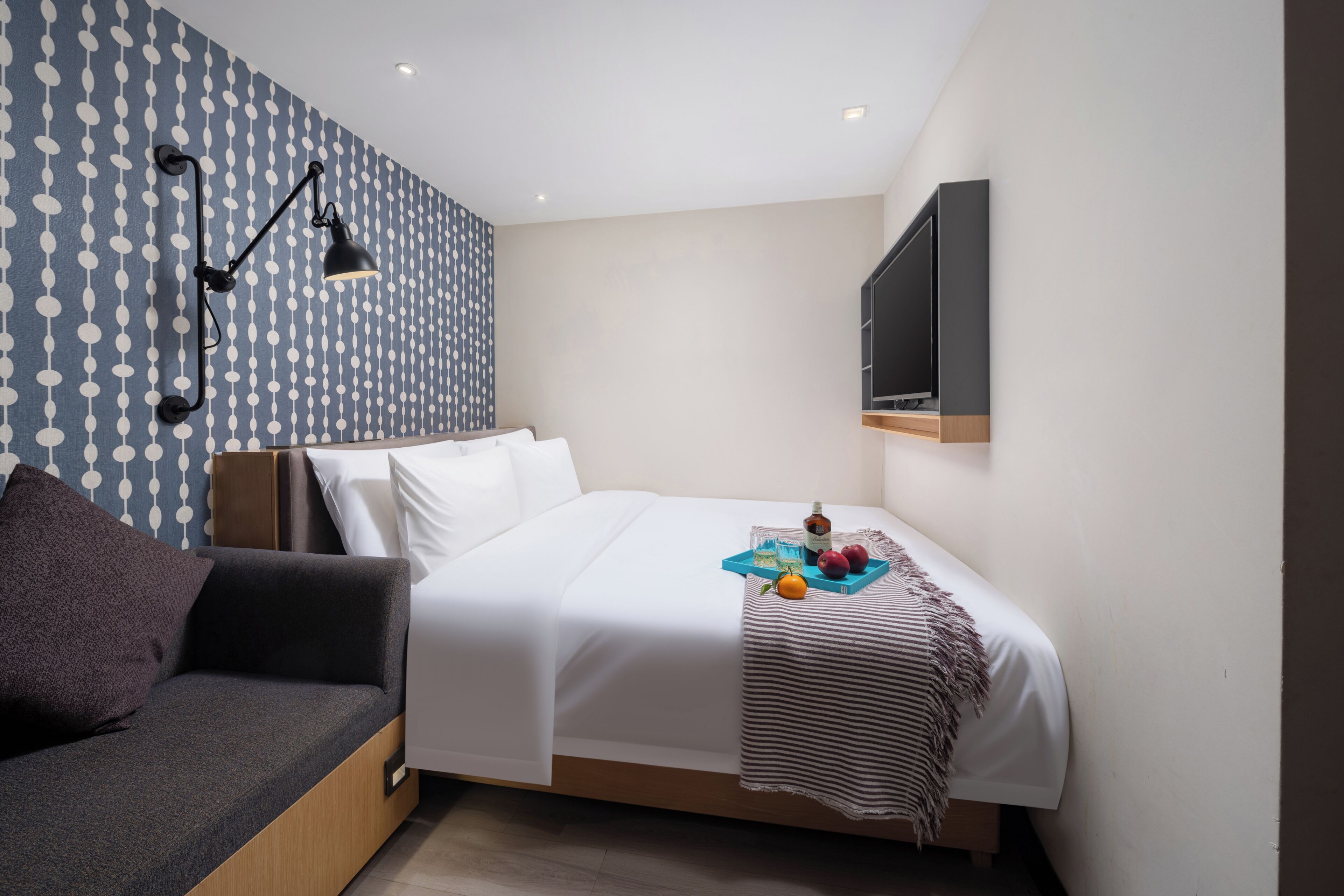 A bedroom with a bed, a sofa, a wall-mounted TV, and a wall lamp.