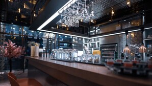 Una zona de bar con una barra larga, varios vasos y una lámpara colgante.