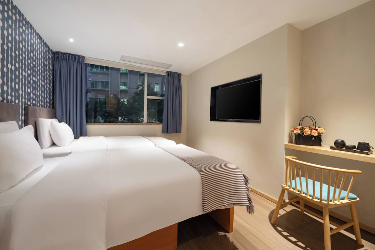 A hotel room with a bed, a desk, a chair, a TV, and a window with curtains.