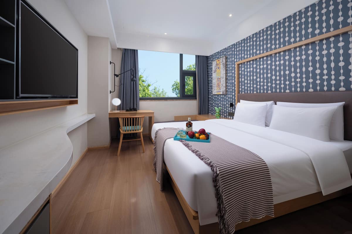 A hotel room with a bed, a desk, a chair, and a large window.