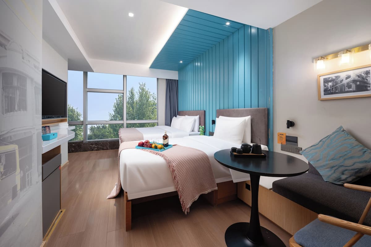 A modern hotel room with a bed, a small table, a sofa, a TV, and a window with a view.