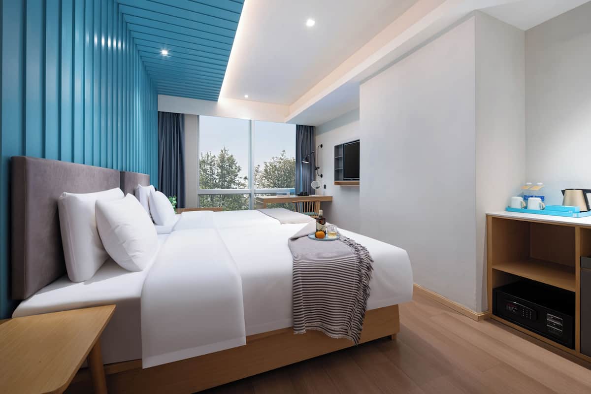 A modern hotel room with a large bed, a desk, a TV, and a view of the outdoors.