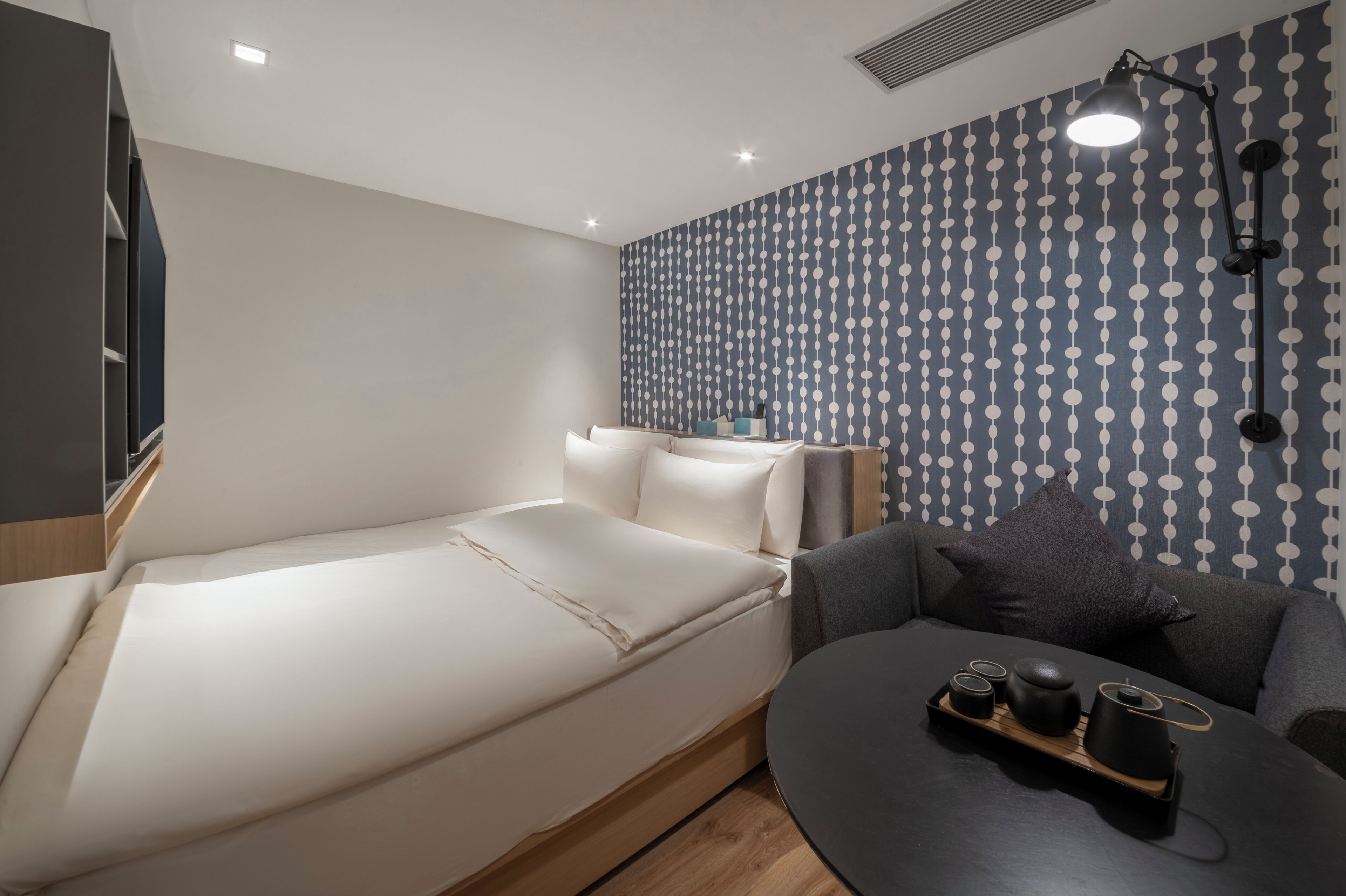 A modern room with a bed, a sofa, a small table with a tray, and a wall with a patterned wallpaper.