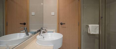 Un baño con dos lavamanos, un espejo y cabina de ducha con paredes de vidrio.