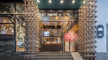 A hotel entrance with a staircase, a reception desk, and a decorative cherry blossom tree.