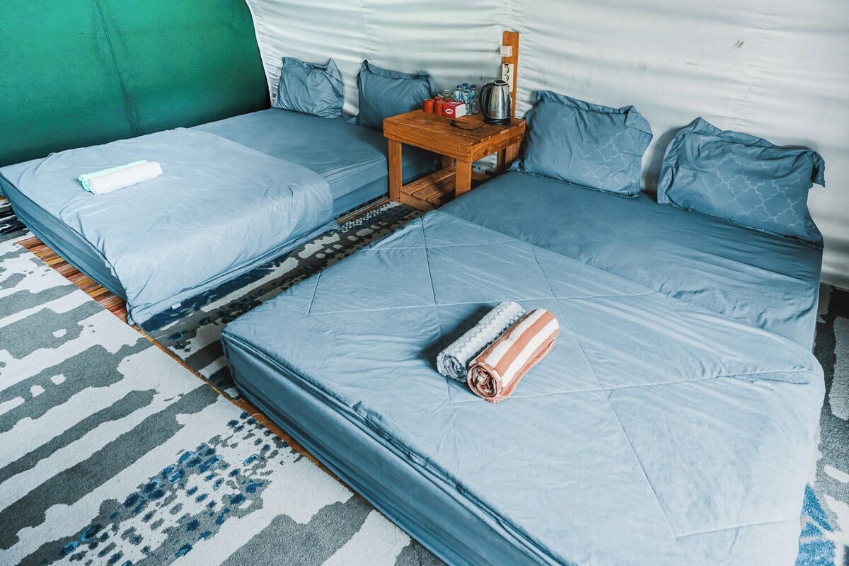 A room with two beds, a small table with a kettle, and a patterned rug.
