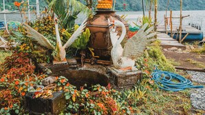 A rustic outdoor setting with a statue, a rustic water feature, and a dock with boats. - Catur Glamping Bedugul (Baturiti)