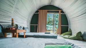 A tent-like room with a bed, a table with items, and a view of greenery outside. - Catur Glamping Bedugul (Baturiti)