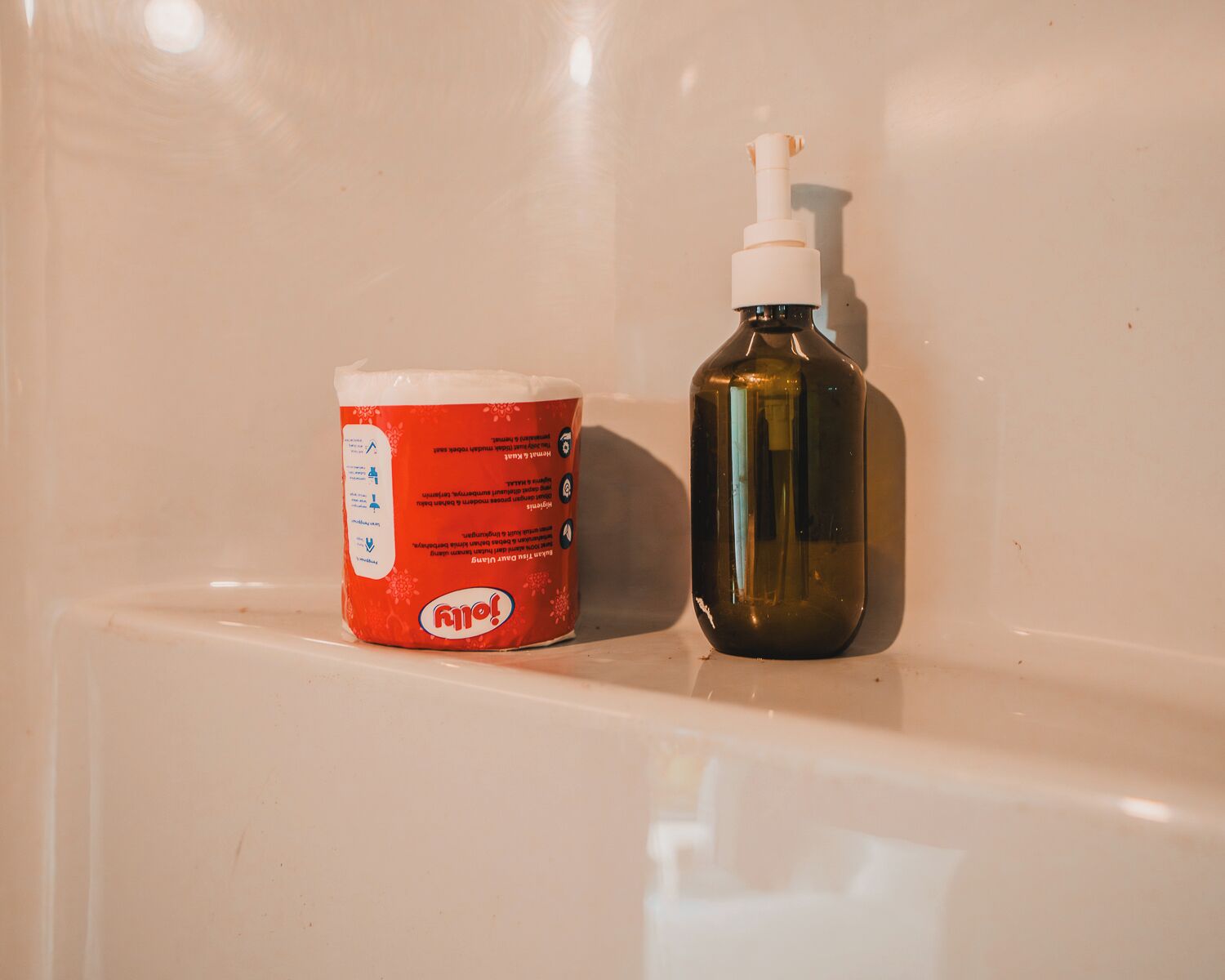 A bathroom with a white sink, a red bottle of Ajax dish soap, and a brown bottle of hand sanitizer.