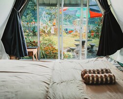 A tented room with a bed, a pillow, and a view of a garden with plants and a fountain.