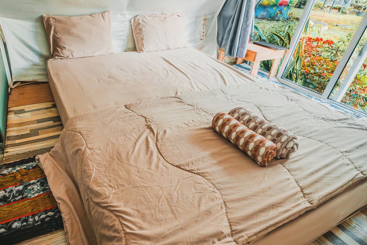 A bed with a beige quilt, pillows, and a rolled towel.