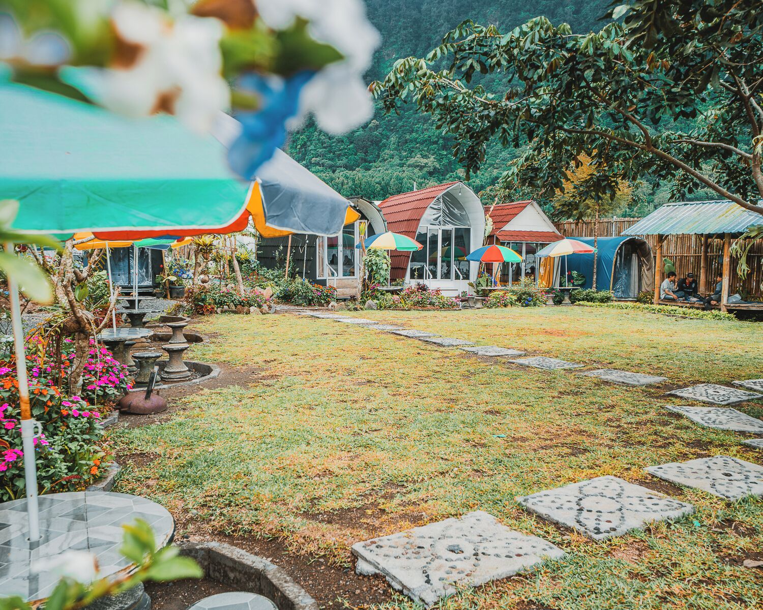 A garden with stone pathways, a gazebo, and a small building with a red roof.