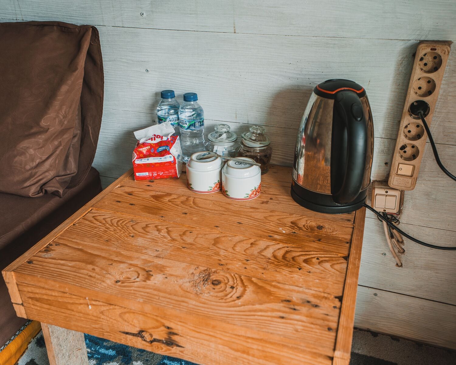 A wooden table with a kettle, water bottles, a tissue box, and jars.