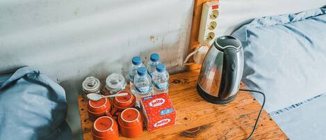 A wooden table with a kettle, water bottles, and orange containers, likely for food storage, against a corrugated metal wall.