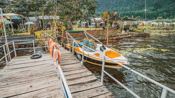 A wooden dock with a boat, surrounded by lush greenery and a forested hill in the background.