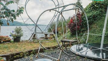 A heart-shaped metal structure with a table and chairs, surrounded by greenery and a body of water.