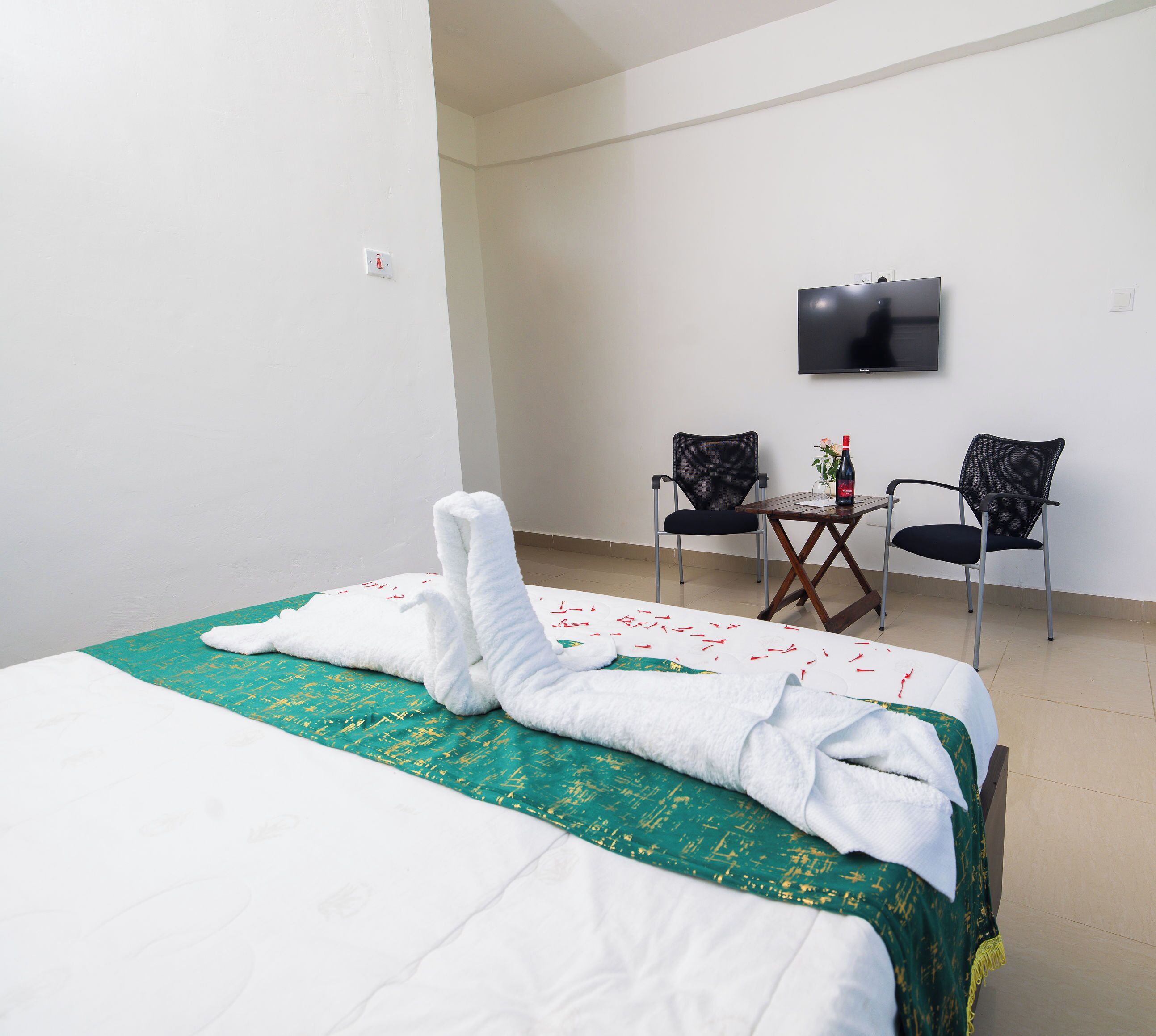 Habitación de hotel con cama, dos sillas, una mesita y un televisor de pantalla plana en la pared.