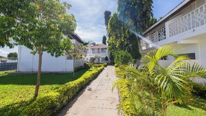 Un sendero que lleva a un edificio de fachada blanca y balcón con celosía.