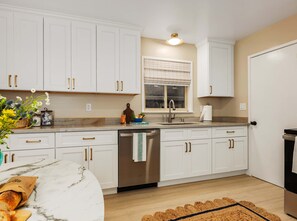 A modern kitchen with white cabinets, a stainless steel dishwasher, and a wooden countertop. - Bay Breeze Bungalow Walk to Cannery Row & Trail (Monterey)
