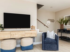 A modern living room with a large flat-screen TV, a wooden console table, a blue armchair, and a staircase. - Bay Breeze Bungalow Walk to Cannery Row & Trail (Monterey)