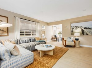 A living room with a sofa, a coffee table, and a dining area with chairs and a table. - Bay Breeze Bungalow Walk to Cannery Row & Trail (Monterey)