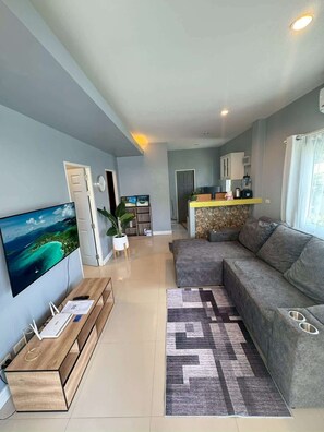 A modern living room with a large flat-screen TV, a sofa, a coffee table, and a kitchen area with cabinets and a countertop. - Villa 9 - Spacious 2 Bedroom Villa with Pool Near Beaches, Dining and Nightlife near Fisherman's Village (Ko Samui District)