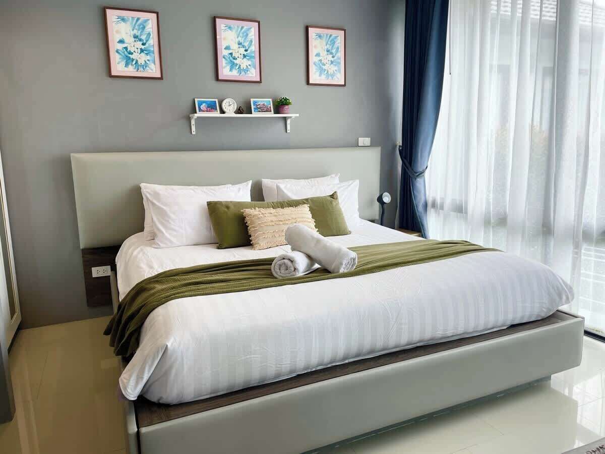 Une chambre d’hôtel moderne avec un grand lit, une table de chevet, une commode et une fenêtre avec des rideaux.