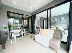 Ein modernes Interieur mit einer Couch, einem Esstisch und Stühlen, einer Küchenzeile und einer großen Schiebeglastür, die in ein Schlafzimmer führt.