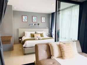 Ein modernes Hotelzimmer mit Bett, einer Couch, einem Schreibtisch und einem großen Fenster mit Vorhängen.